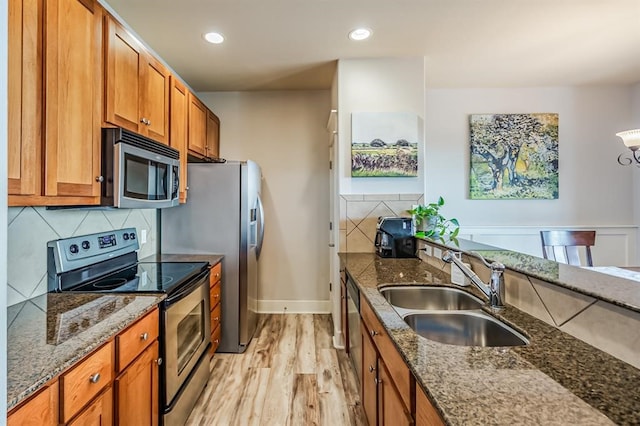 kitchen with backsplash, dark stone counters, stainless steel appliances, sink, and light hardwood / wood-style flooring