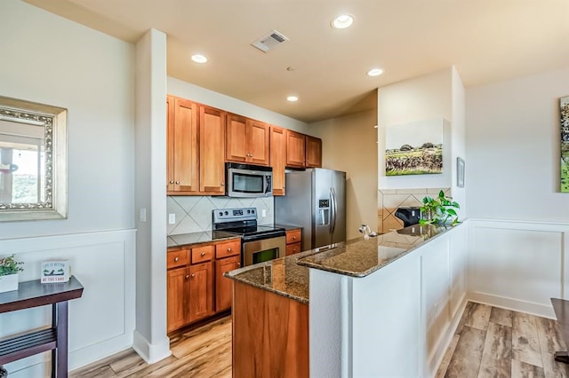 kitchen with dark stone countertops, appliances with stainless steel finishes, tasteful backsplash, light hardwood / wood-style floors, and kitchen peninsula