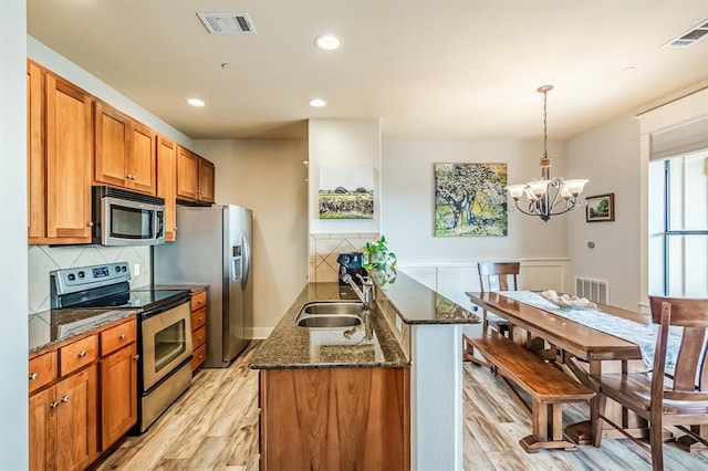 kitchen with decorative backsplash, stainless steel appliances, pendant lighting, light hardwood / wood-style flooring, and a notable chandelier