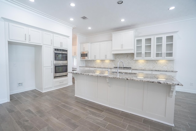 kitchen with stainless steel appliances, white cabinetry, a center island with sink, and light stone countertops