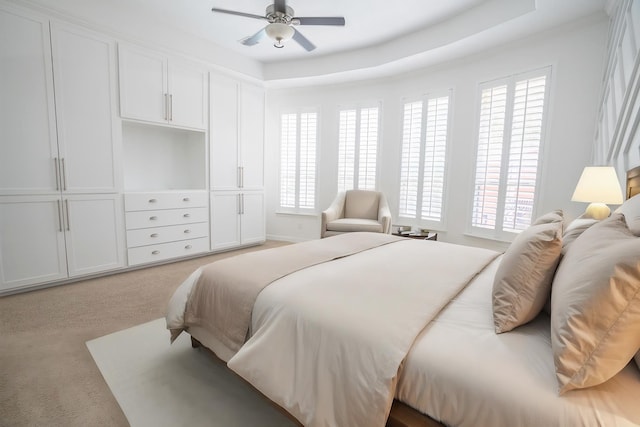 bedroom with a raised ceiling, ceiling fan, and light colored carpet