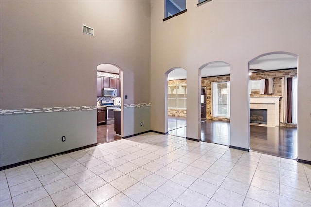 unfurnished room featuring a fireplace, a towering ceiling, and light tile patterned flooring