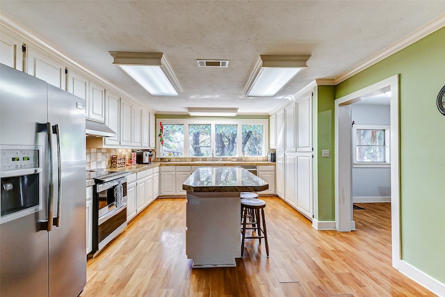 kitchen with a kitchen bar, stainless steel appliances, a kitchen island, and a wealth of natural light