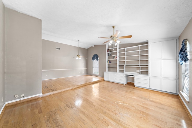 unfurnished living room with light wood-type flooring, built in desk, vaulted ceiling, and a healthy amount of sunlight