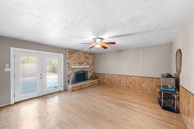 unfurnished living room featuring wood walls, a fireplace, a textured ceiling, ceiling fan, and light wood-type flooring