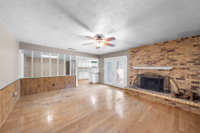 unfurnished living room featuring wooden walls, light hardwood / wood-style floors, a textured ceiling, and a brick fireplace