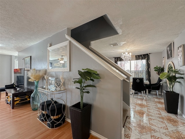 corridor featuring a notable chandelier, a textured ceiling, and light wood-type flooring