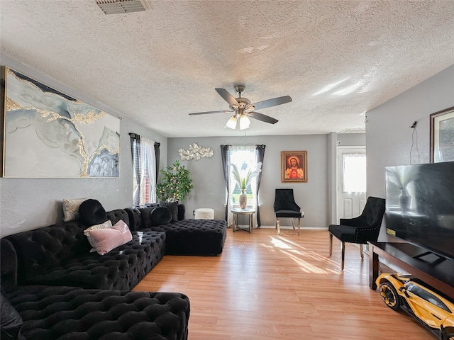 living room featuring ceiling fan, light hardwood / wood-style floors, and a textured ceiling