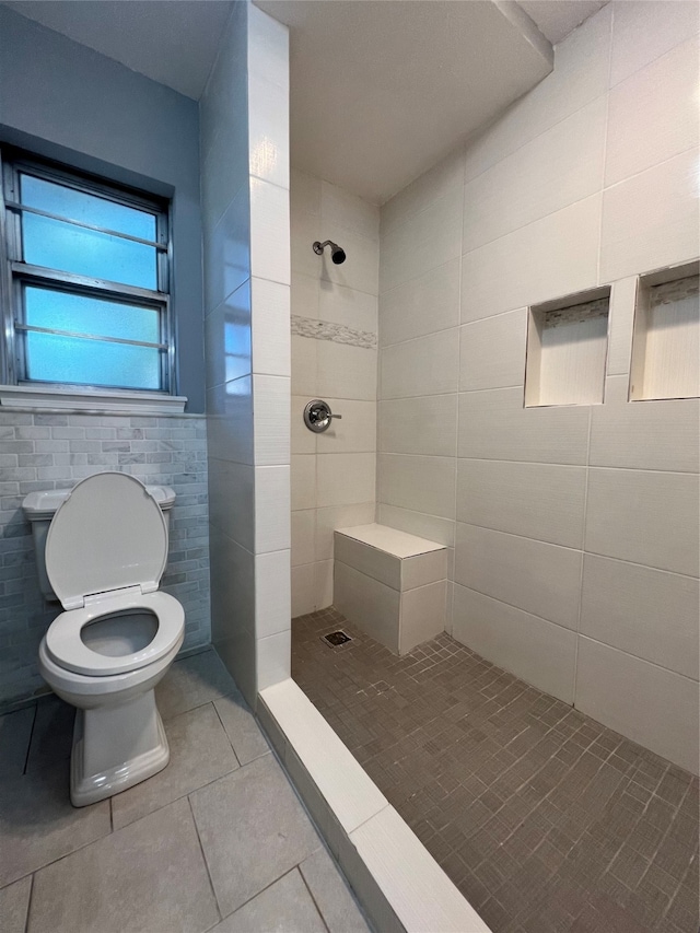 bathroom featuring a tile shower, tile patterned flooring, tile walls, and toilet