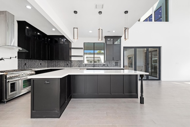 kitchen featuring a spacious island, wall chimney exhaust hood, range with two ovens, and hanging light fixtures