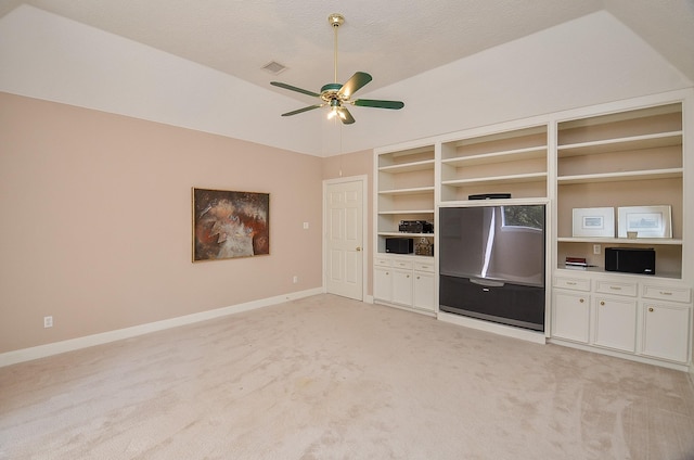 unfurnished living room featuring built in shelves, light colored carpet, vaulted ceiling, a textured ceiling, and ceiling fan