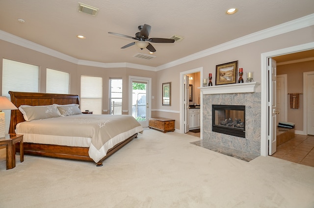 bedroom with connected bathroom, light carpet, ornamental molding, a tile fireplace, and ceiling fan