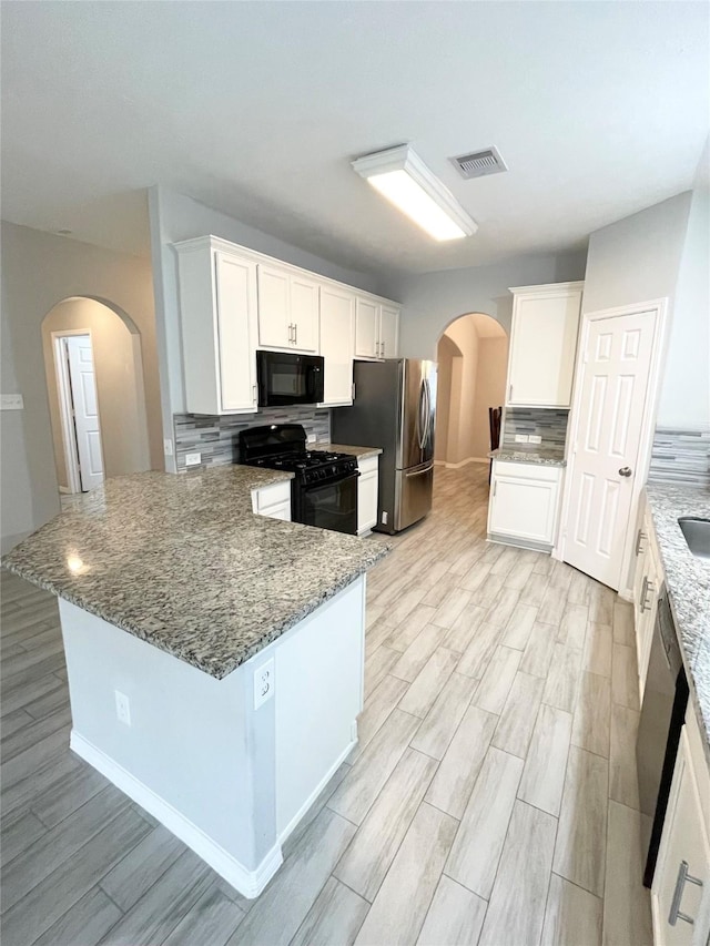 kitchen with stone counters, black appliances, white cabinets, decorative backsplash, and light hardwood / wood-style floors