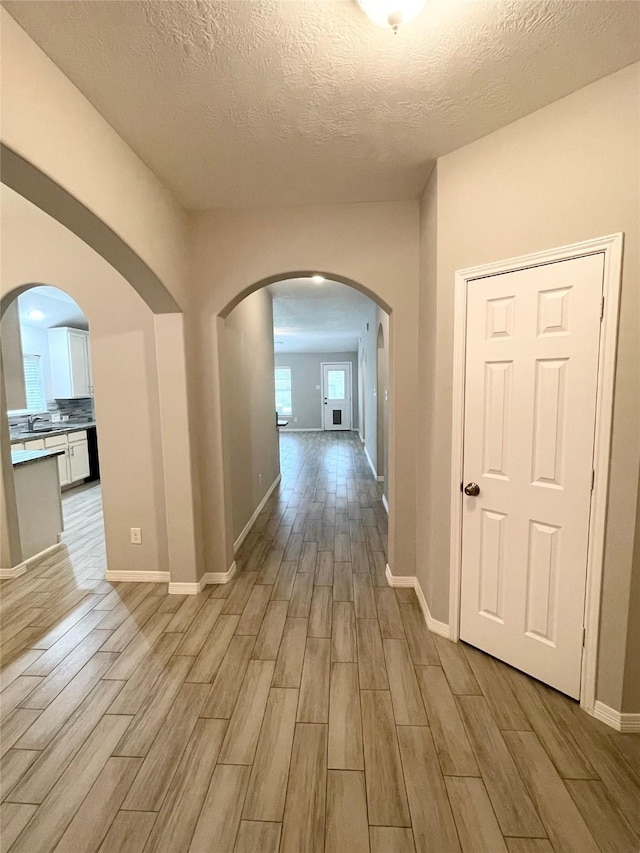 hallway featuring sink, a textured ceiling, and light hardwood / wood-style flooring