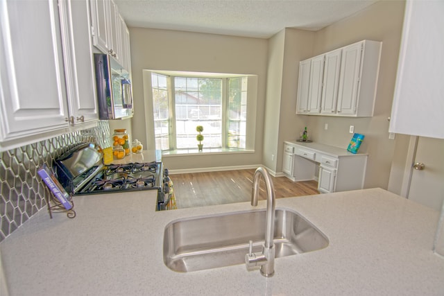 kitchen with gas range, light hardwood / wood-style flooring, white cabinets, and sink