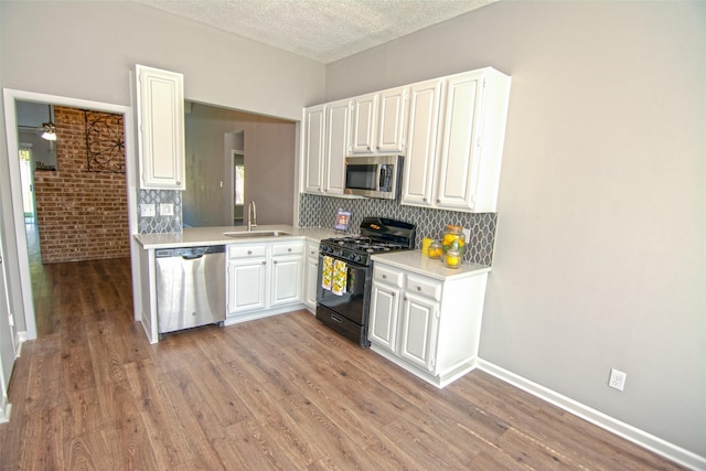 kitchen featuring brick wall, appliances with stainless steel finishes, hardwood / wood-style floors, white cabinetry, and sink