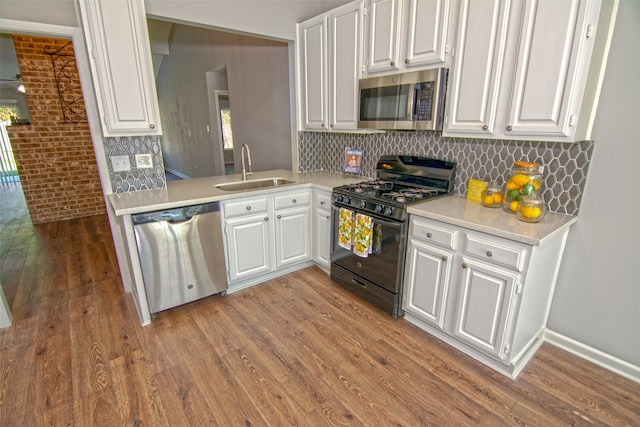 kitchen featuring brick wall, sink, white cabinetry, and stainless steel appliances