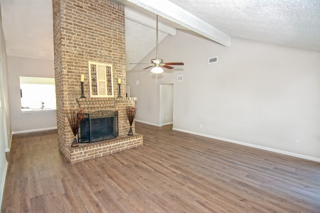 unfurnished living room featuring a textured ceiling, wood-type flooring, a brick fireplace, beamed ceiling, and ceiling fan