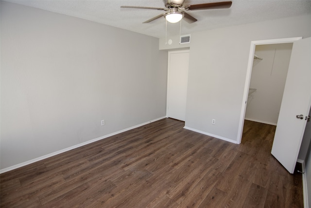 unfurnished bedroom featuring dark wood-type flooring, ceiling fan, a walk in closet, and a closet