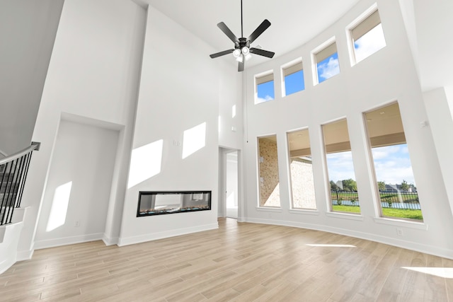 unfurnished living room featuring a high ceiling, a multi sided fireplace, ceiling fan, and light hardwood / wood-style flooring