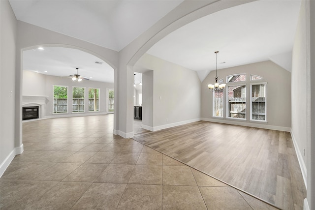 unfurnished living room with ceiling fan with notable chandelier, light wood-type flooring, and vaulted ceiling