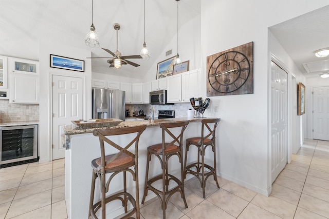 kitchen with kitchen peninsula, wine cooler, light stone countertops, appliances with stainless steel finishes, and white cabinetry