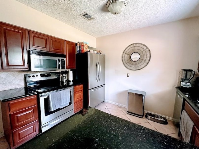 kitchen featuring dark stone countertops, light tile patterned floors, stainless steel appliances, and a textured ceiling