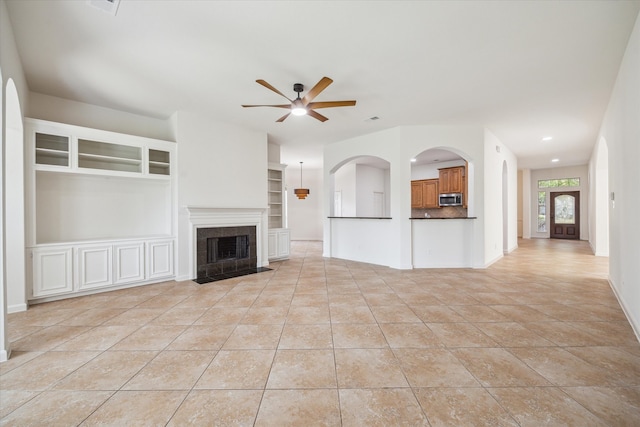 unfurnished living room with a fireplace, built in shelves, light tile patterned floors, and ceiling fan