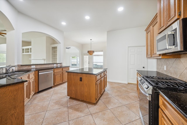 kitchen with appliances with stainless steel finishes, backsplash, sink, decorative light fixtures, and a center island