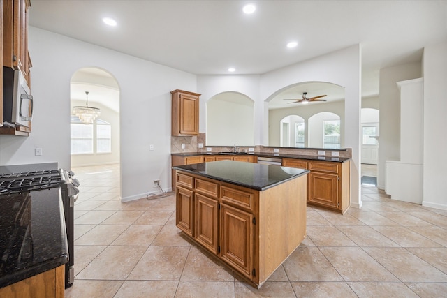 kitchen featuring ceiling fan with notable chandelier, stainless steel appliances, a kitchen island, and dark stone countertops