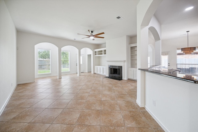 unfurnished living room with built in shelves, ceiling fan, and light tile patterned floors