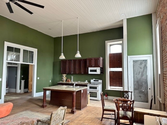 kitchen with a kitchen bar, hanging light fixtures, white appliances, dark brown cabinets, and light wood-type flooring