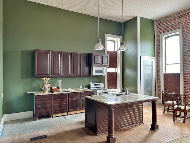 kitchen with light hardwood / wood-style flooring, brick wall, pendant lighting, white appliances, and dark brown cabinets