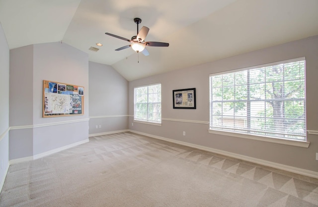 empty room featuring ceiling fan, light colored carpet, vaulted ceiling, and a wealth of natural light