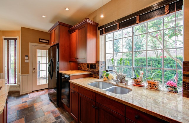 kitchen featuring black appliances, sink, hanging light fixtures, backsplash, and light stone counters