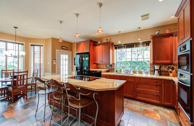 kitchen featuring a kitchen bar, hanging light fixtures, a kitchen island, black appliances, and sink