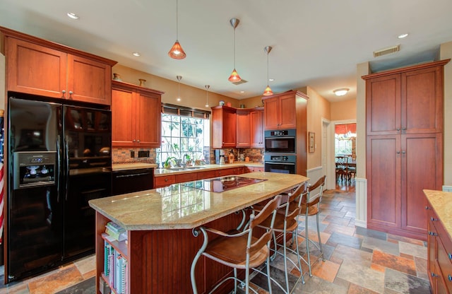 kitchen with decorative backsplash, light stone countertops, black appliances, and a center island