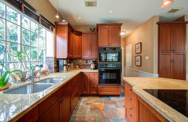 kitchen with tasteful backsplash, sink, hanging light fixtures, light stone countertops, and black appliances