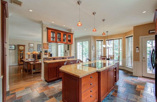 kitchen with a kitchen island, decorative light fixtures, black electric stovetop, an inviting chandelier, and light stone counters