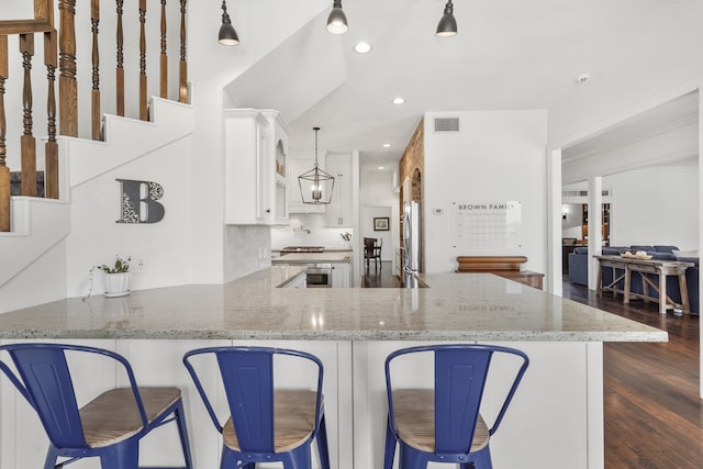 kitchen featuring hanging light fixtures, dark hardwood / wood-style floors, kitchen peninsula, stainless steel fridge, and white cabinets