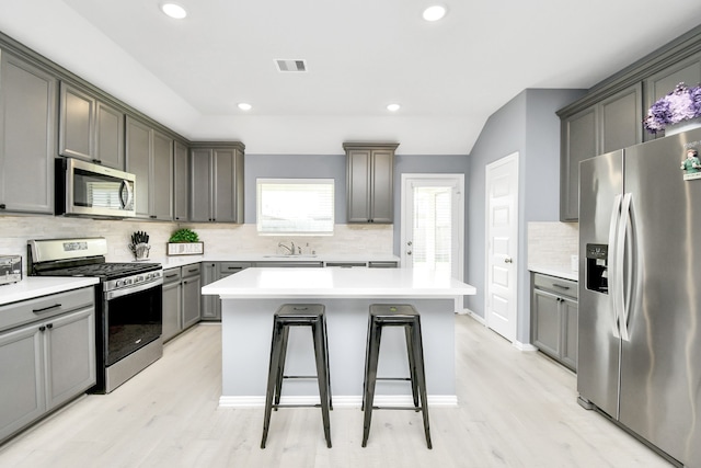 kitchen with decorative backsplash, gray cabinetry, stainless steel appliances, light hardwood / wood-style floors, and a kitchen island