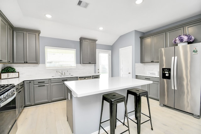 kitchen with decorative backsplash, appliances with stainless steel finishes, a breakfast bar, vaulted ceiling, and light hardwood / wood-style flooring