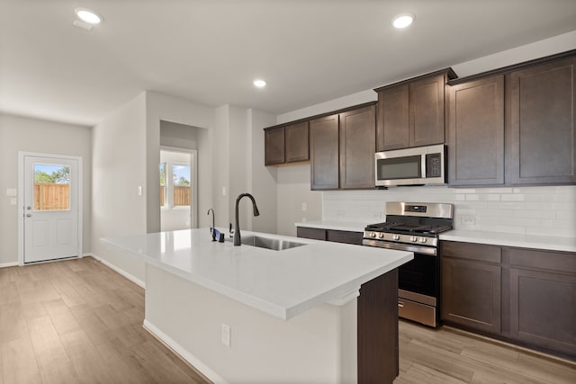 kitchen with appliances with stainless steel finishes, tasteful backsplash, sink, a center island with sink, and light hardwood / wood-style floors