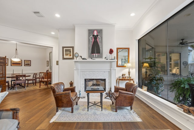 living room with hardwood / wood-style floors, ceiling fan, crown molding, and a tiled fireplace