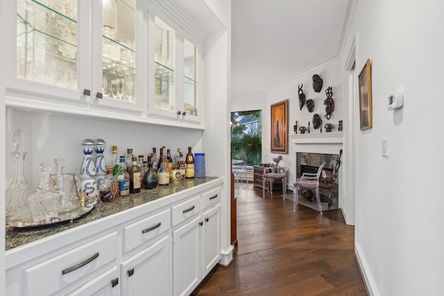 bar featuring dark hardwood / wood-style flooring, white cabinetry, a fireplace, and ornamental molding