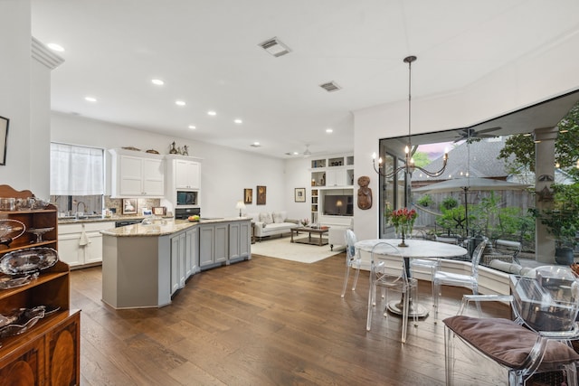 kitchen with light stone counters, ceiling fan with notable chandelier, dark wood-type flooring, decorative light fixtures, and white cabinetry