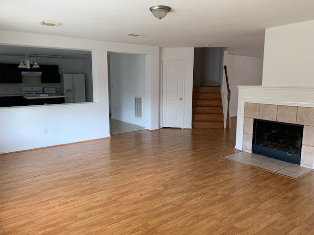 unfurnished living room with light hardwood / wood-style flooring, a notable chandelier, and a tiled fireplace