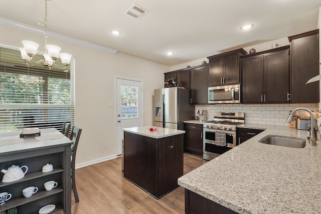 kitchen with sink, appliances with stainless steel finishes, hanging light fixtures, a center island, and light stone countertops