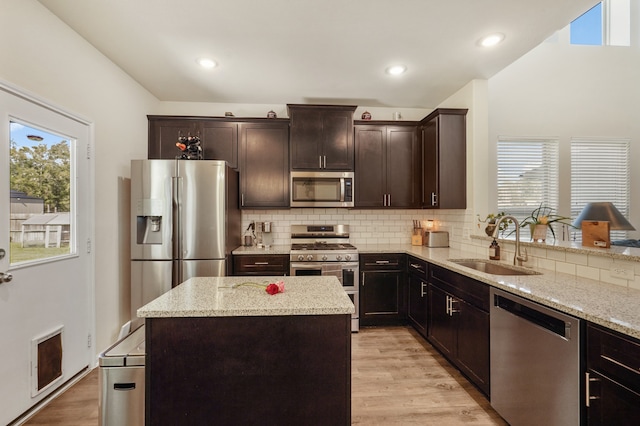 kitchen with sink, stainless steel appliances, light stone counters, a kitchen island, and light wood-type flooring