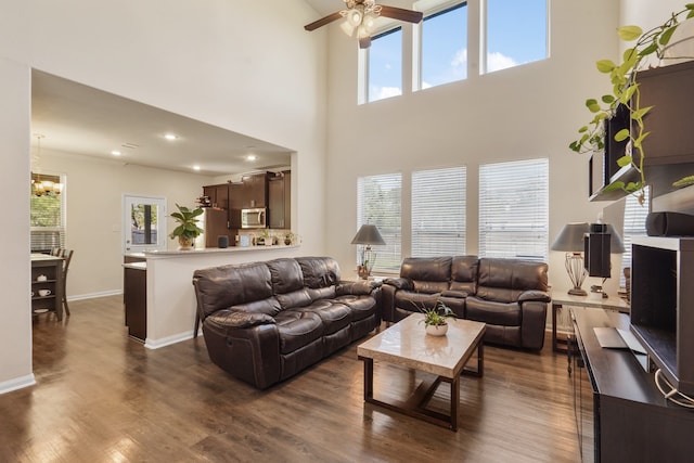 living room featuring dark hardwood / wood-style flooring, ceiling fan with notable chandelier, and a towering ceiling